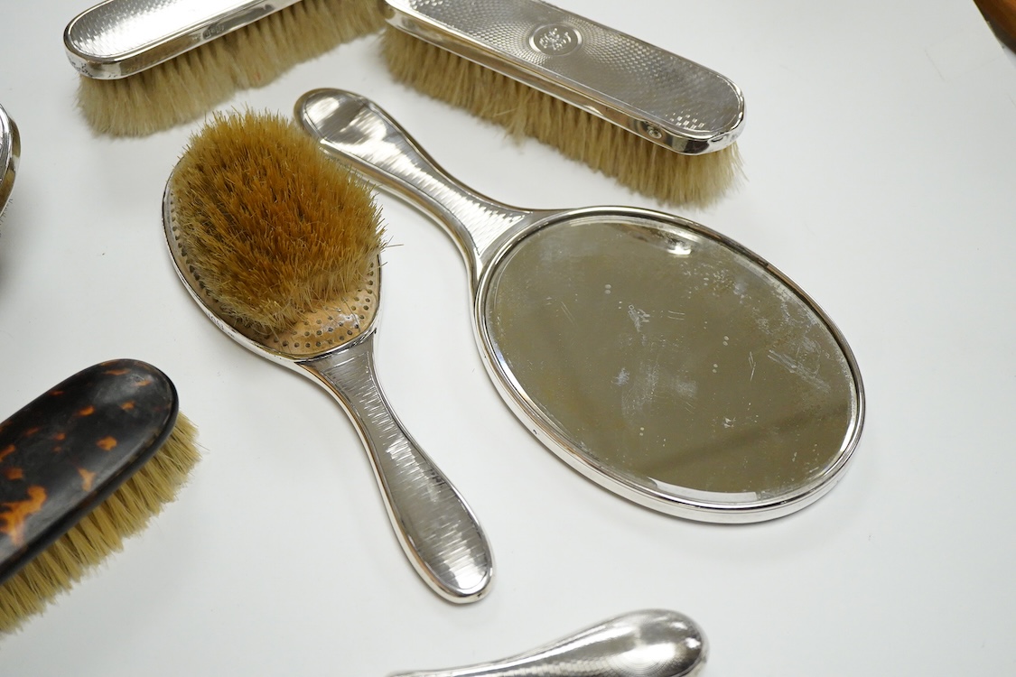 A George V seven piece silver mounted toilet set by Charles Henry Dumenil, comprising a hand mirror, four brushes, a glass toilet jar and button hook, London, 1911/12 & 18, together with one other silver mounted toilet j